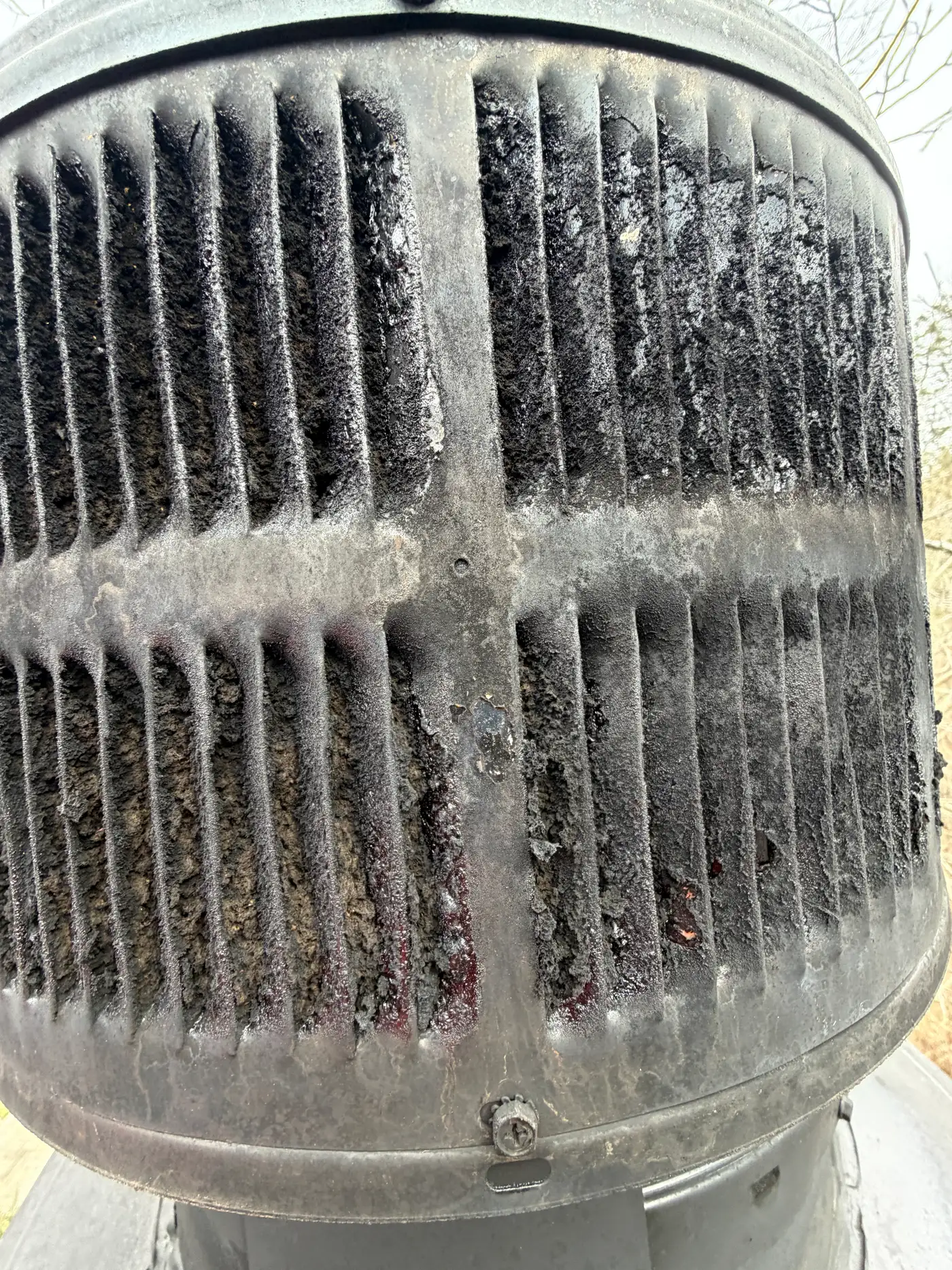 Expanded carbonized creosote choking the chimney cap screen after a hidden chimney fire — Crestwood, KY