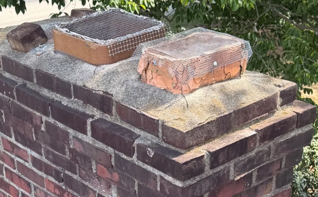 Two clay flue tiles wrapped in wire mesh and a loose brick on a cracked concrete chimney crown — Rolling Lane, St. Matthews, KY